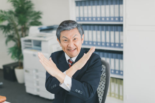鬼の形相でバツを作るスーツ姿の男性